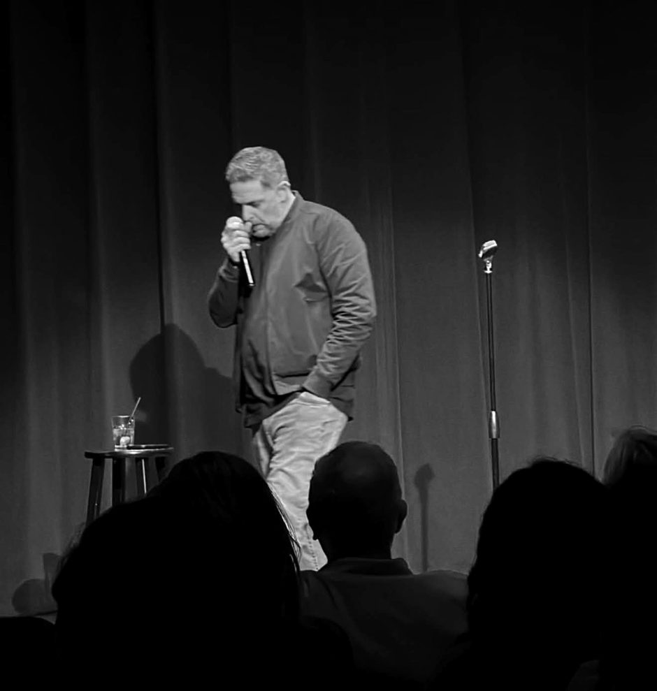 Gary Bolles on stage with a microphone in front of a red curtain