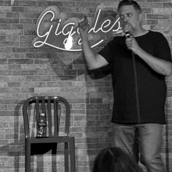 Gary Bolles on stage under a neon Giggles sign